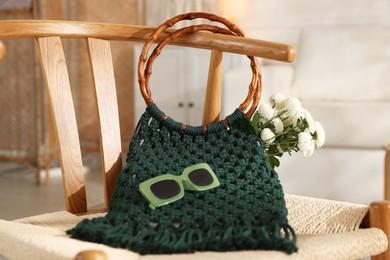 Photo of Handmade macrame shopping bag with flowers and sunglasses on chair indoors