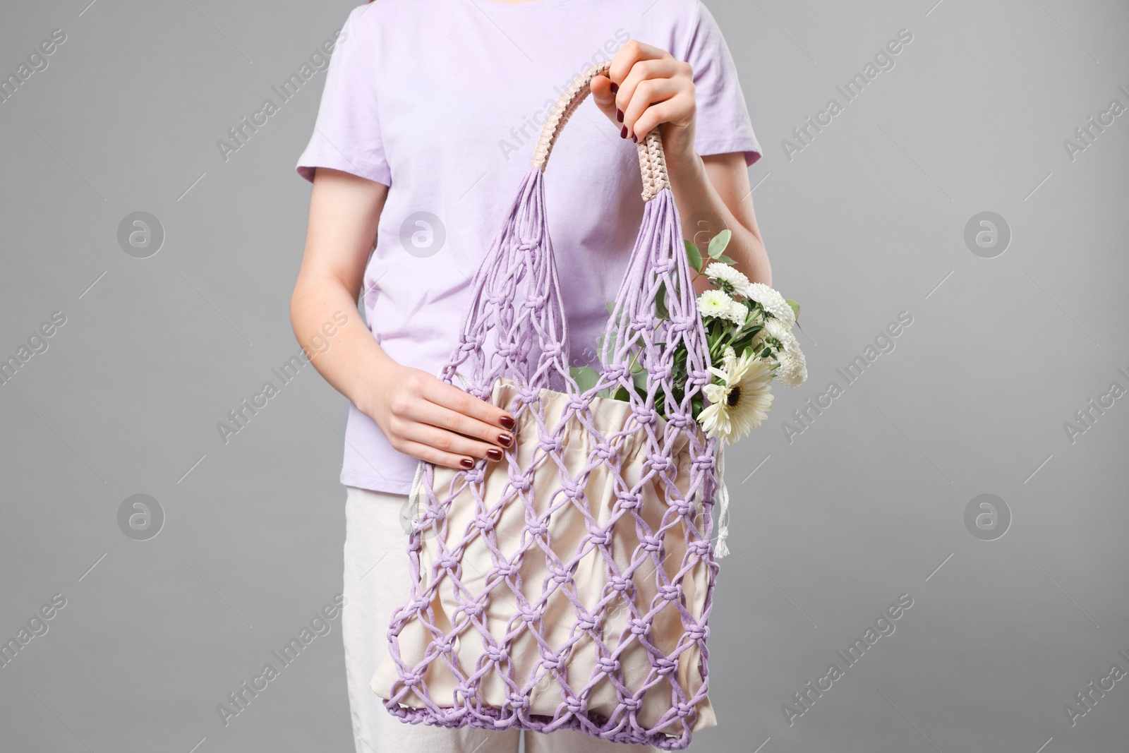 Photo of Teenage girl with handmade macrame bag on grey background, closeup