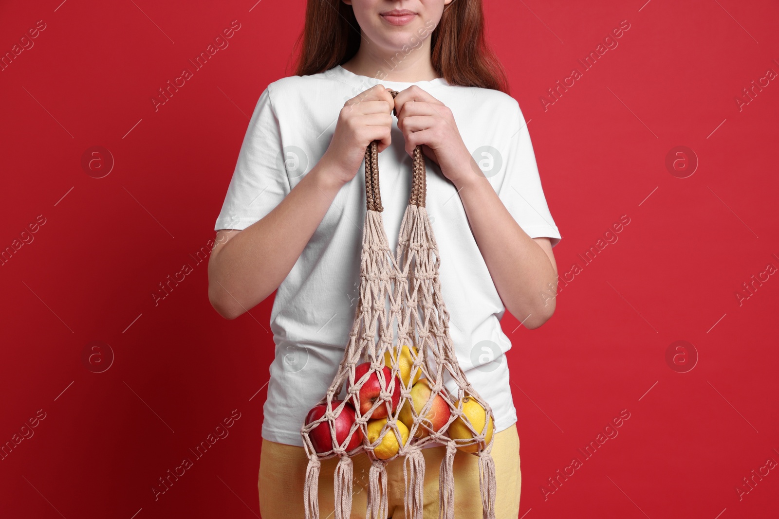 Photo of Teenage girl with handmade macrame bag on red background, closeup