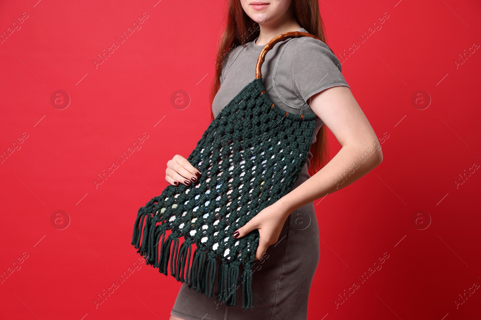 Photo of Teenage girl with handmade macrame bag on red background, closeup