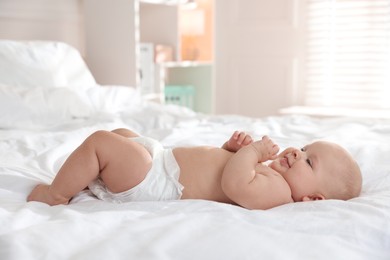 Photo of Cute little baby in diaper on bed indoors