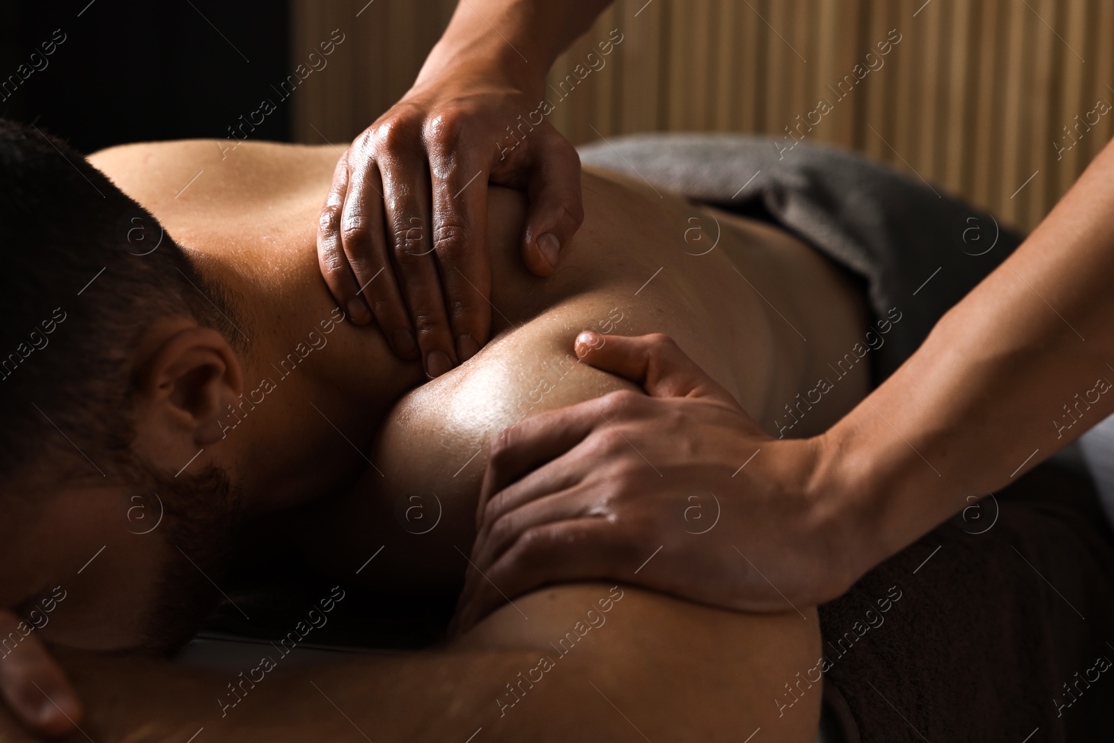 Photo of Professional physiotherapist doing shoulder massage for his client indoors, closeup