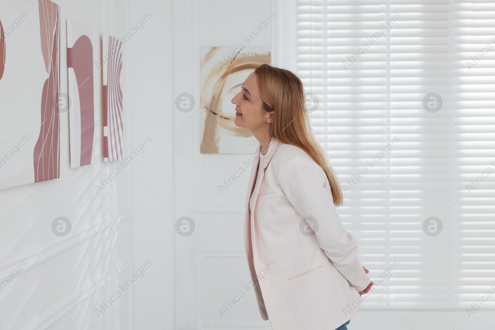 Photo of Woman examining beautiful paintings in art gallery