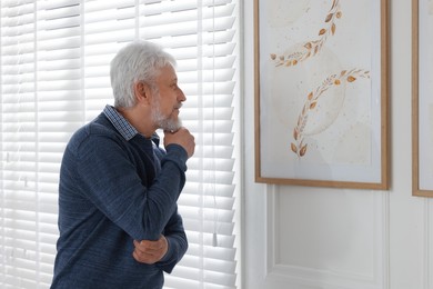 Photo of Senior man examining beautiful paintings in art gallery