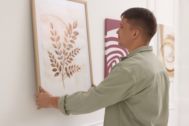 Photo of Man hanging painting on wall in art gallery