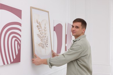 Photo of Man hanging painting on wall in art gallery