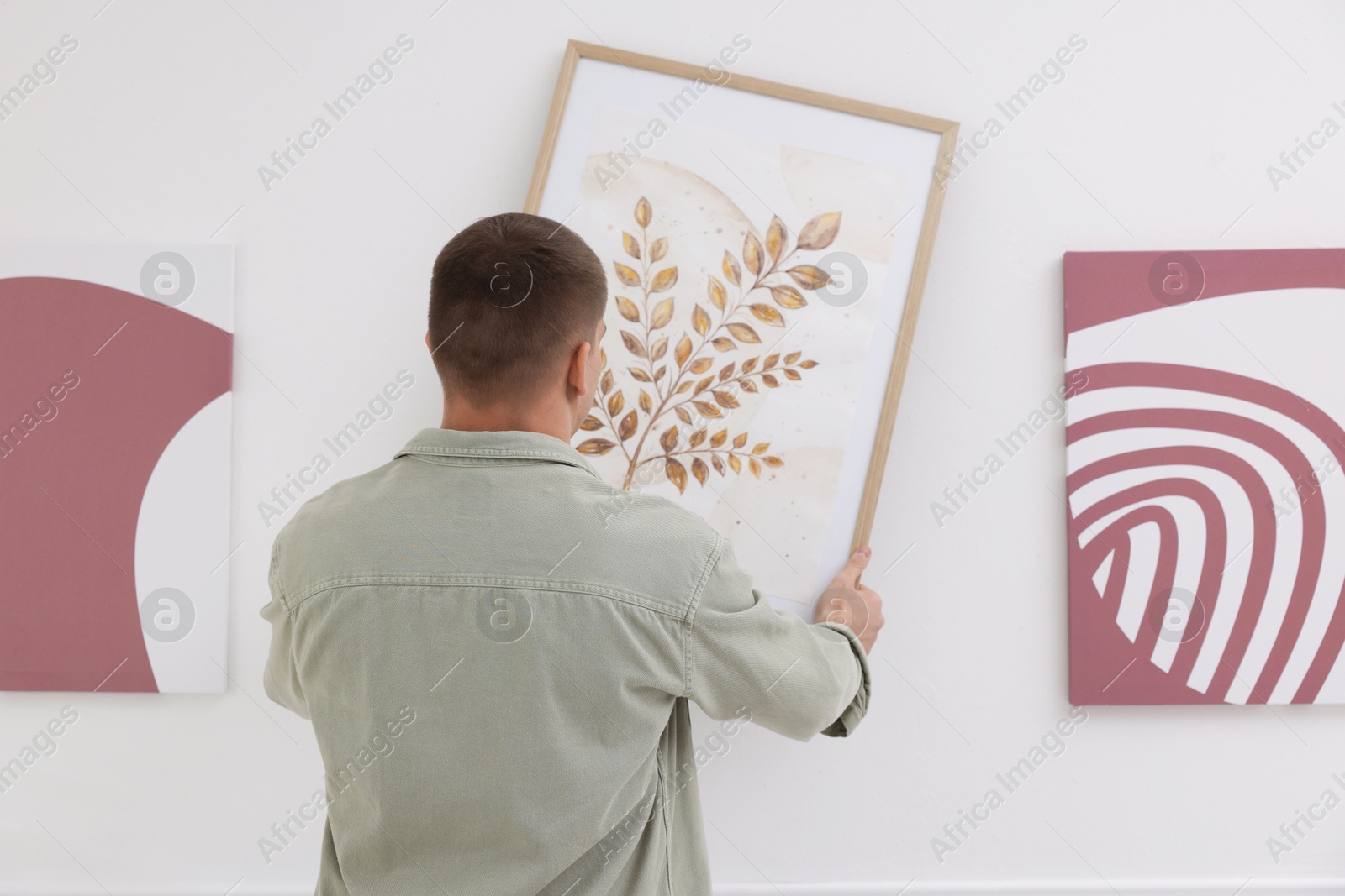 Photo of Man hanging painting on wall in art gallery, back view