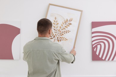 Photo of Man hanging painting on wall in art gallery, back view