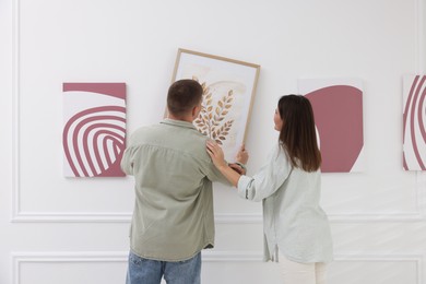 Photo of Man and woman hanging paintings on wall in art gallery, back view