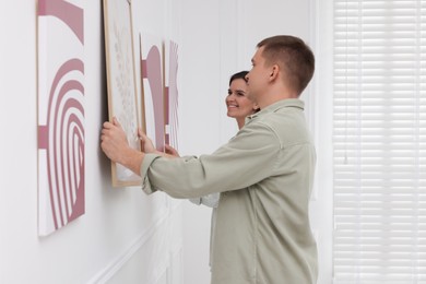 Photo of Man and woman hanging paintings on wall in art gallery