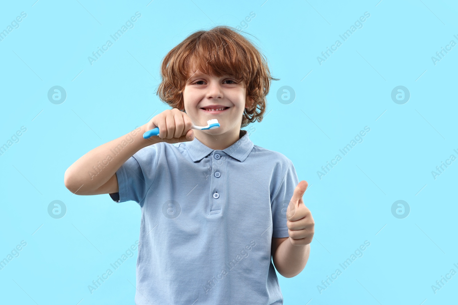 Photo of Cute boy with toothbrush showing thumbs up on light blue background