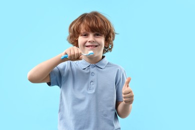 Photo of Cute boy with toothbrush showing thumbs up on light blue background