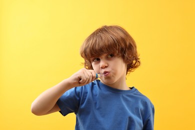 Photo of Cute boy brushing his teeth on yellow background