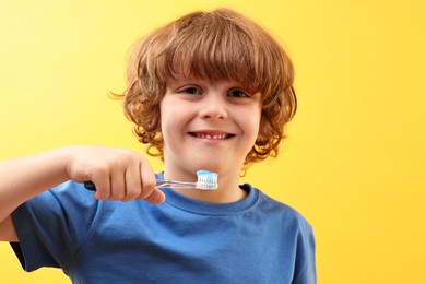 Cute boy with toothbrush and paste on yellow background