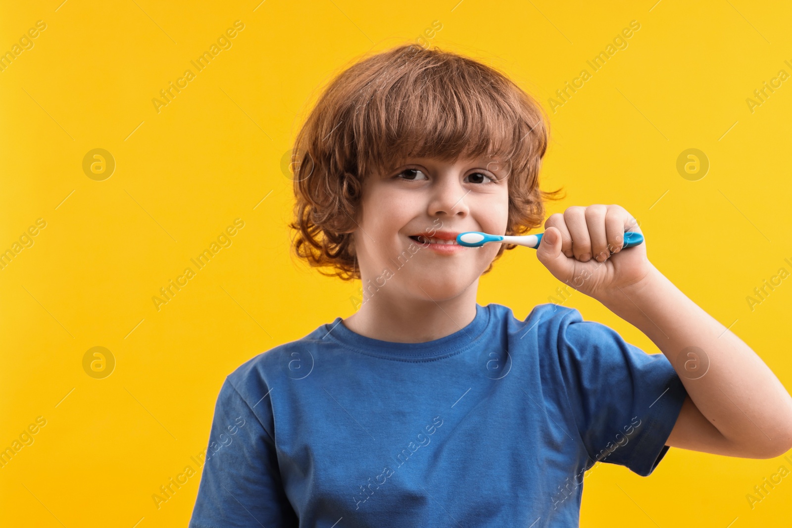 Photo of Cute boy brushing his teeth on yellow background