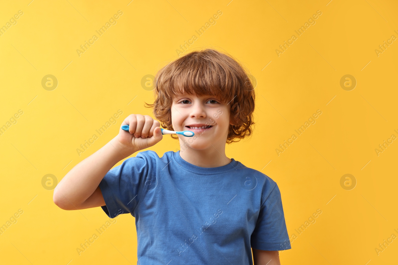 Photo of Cute boy brushing his teeth on yellow background