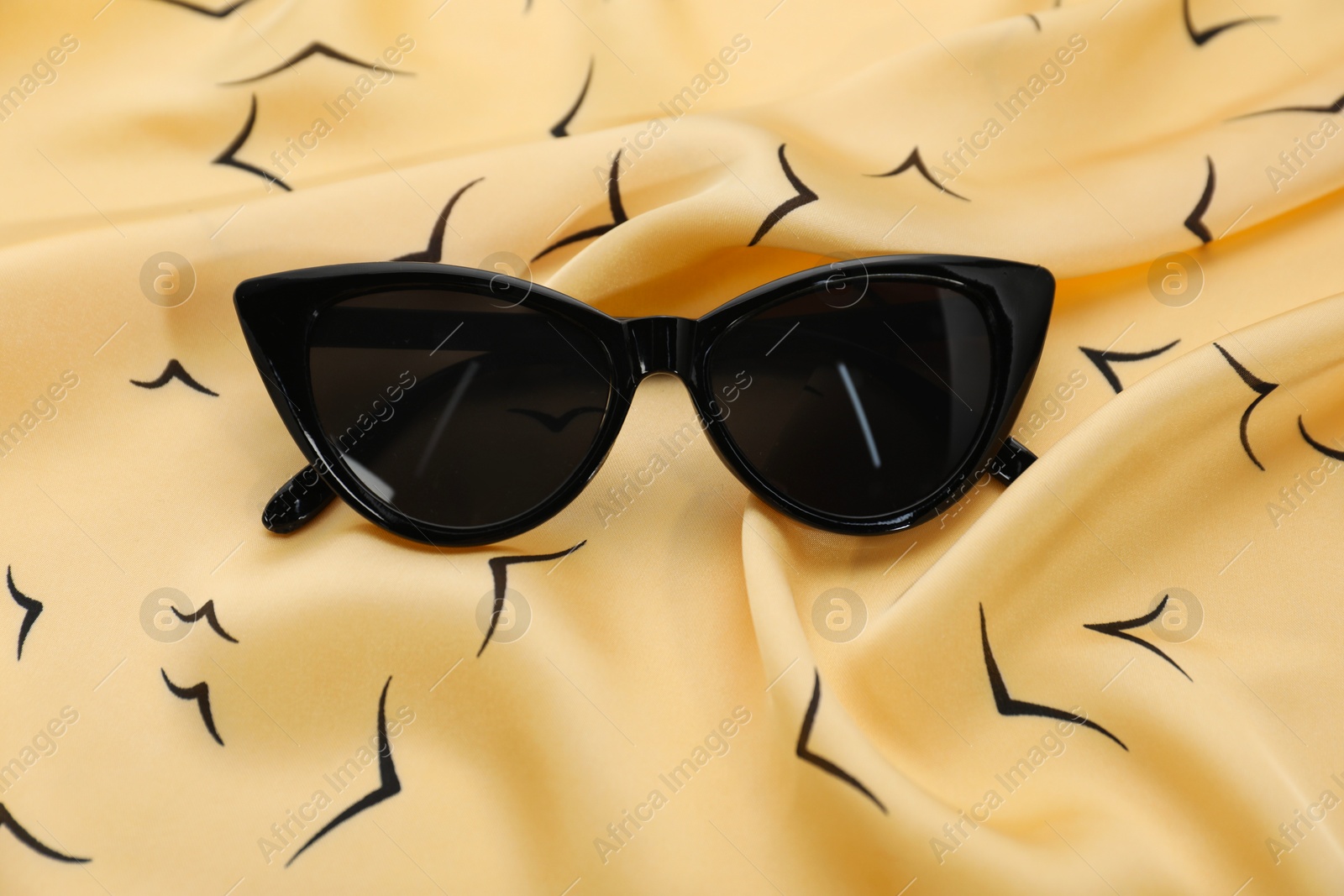 Photo of Stylish sunglasses on beige fabric. Elegant accessory