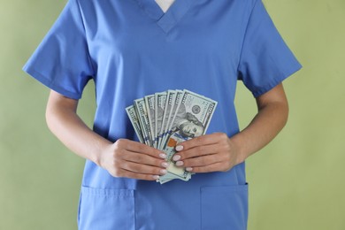 Photo of Corruption concept. Doctor with dollar banknotes on green background, closeup