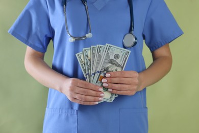 Photo of Corruption concept. Doctor with dollar banknotes on green background, closeup