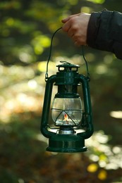 Photo of Woman holding vintage kerosene lamp in forest at evening, closeup