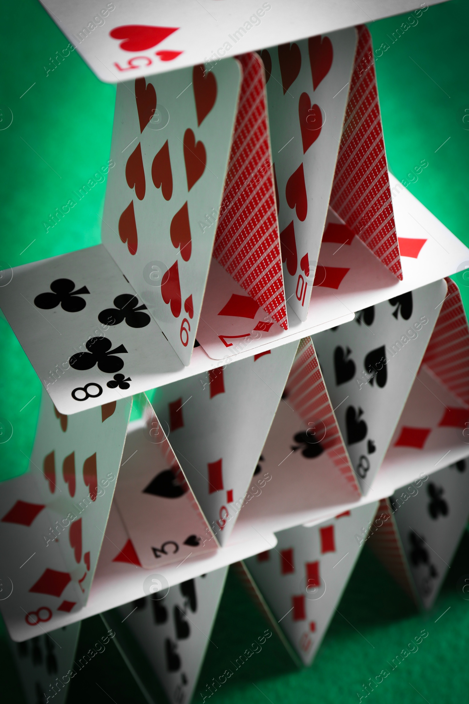 Photo of House of playing cards on green background, closeup