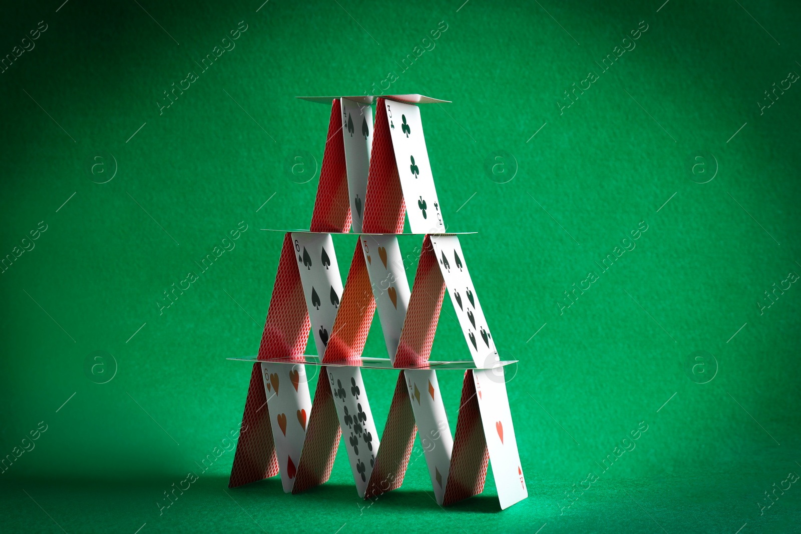 Photo of House of playing cards on green background