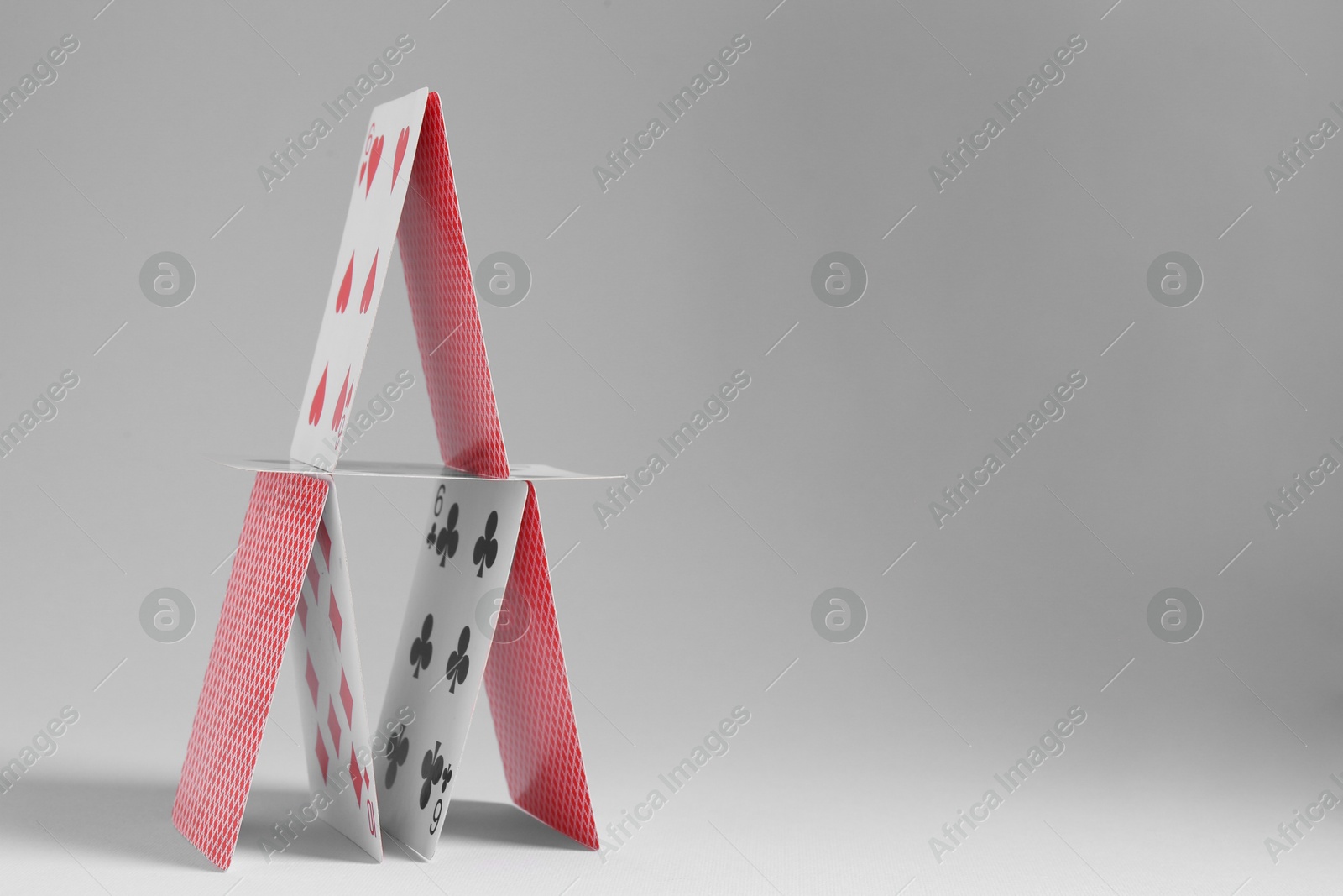 Photo of House of playing cards on light grey background. Space for text