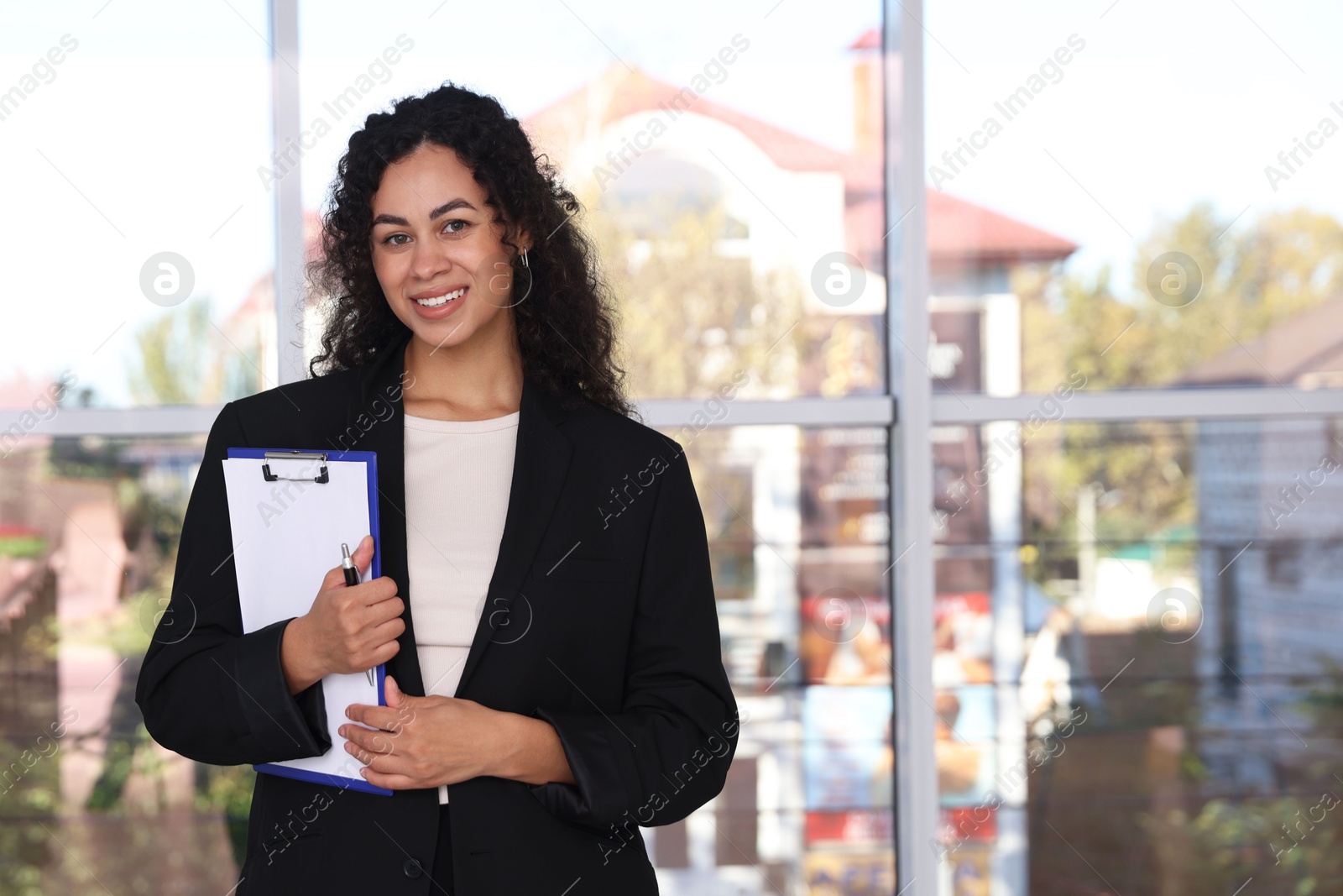 Photo of Portrait of young woman with clipboard wearing stylish suit indoors. Space for text