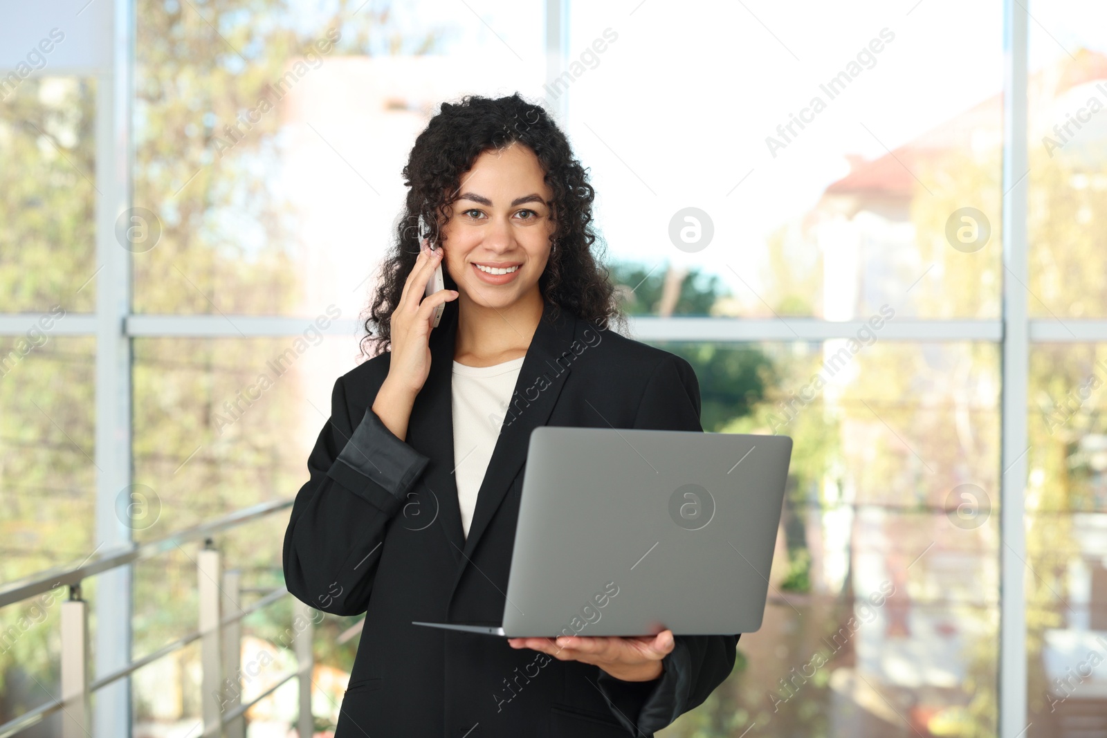 Photo of Portrait of young woman with laptop and phone wearing stylish suit indoors