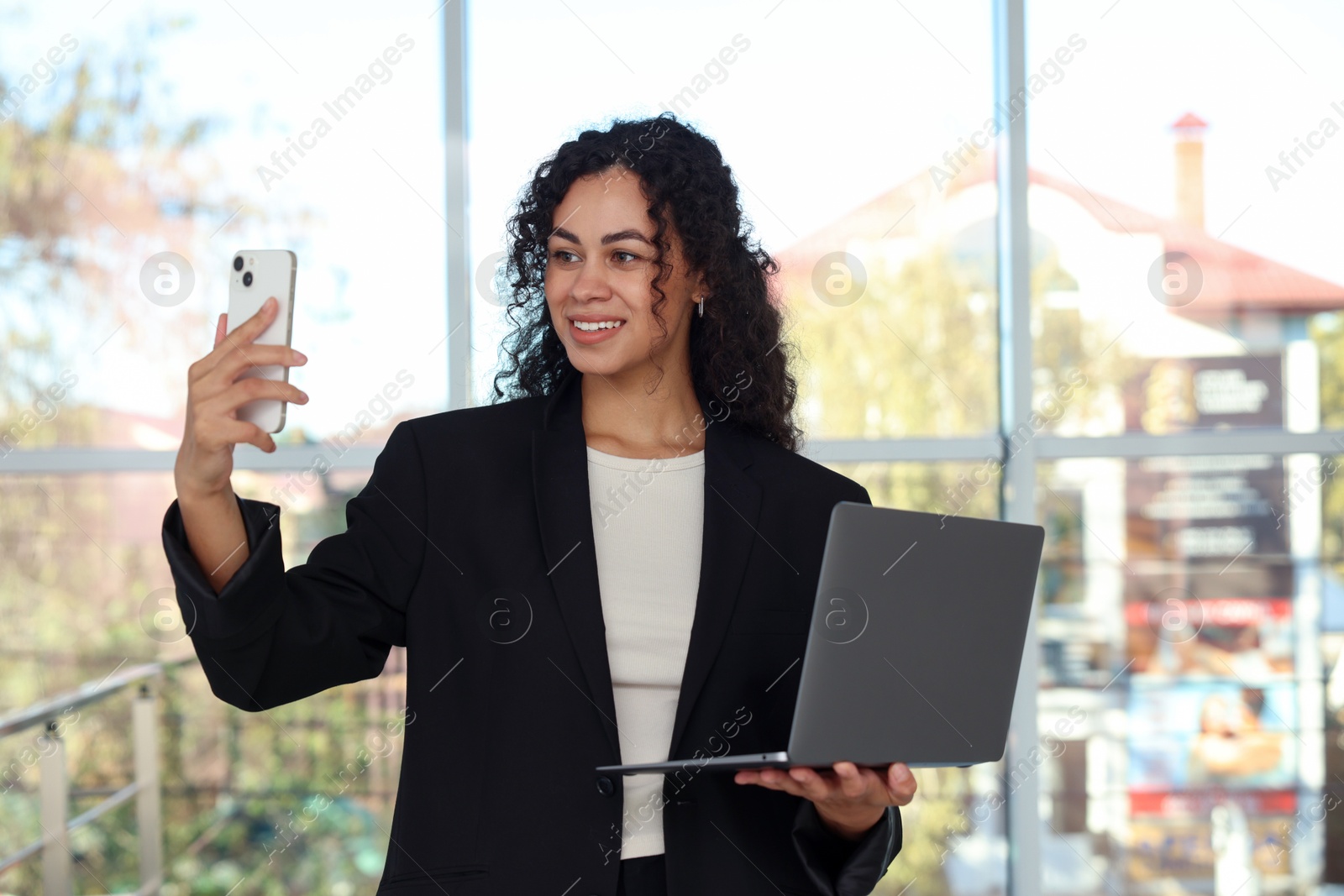 Photo of Portrait of young woman with laptop and phone wearing stylish suit indoors