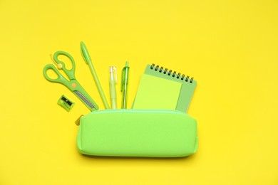 Photo of Pencil case and different stationery on yellow background, flat lay