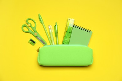Photo of Pencil case and different stationery on yellow background, flat lay