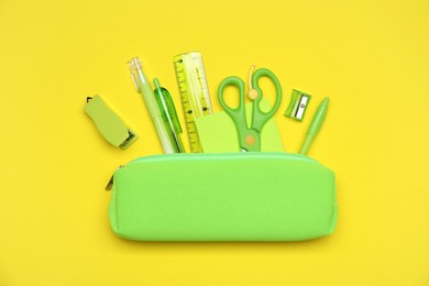 Photo of Pencil case and different stationery on yellow background, flat lay
