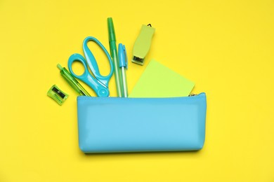 Photo of Pencil case and different stationery on yellow background, flat lay