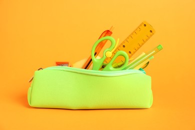 Photo of Different stationery in pencil case on orange background