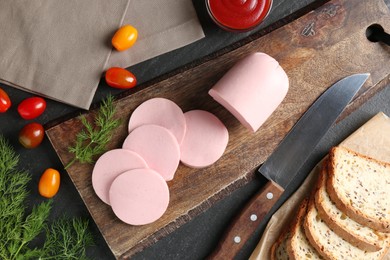 Photo of Tasty boiled sausage, knife, tomatoes, dill, bread and ketchup on black table, top view