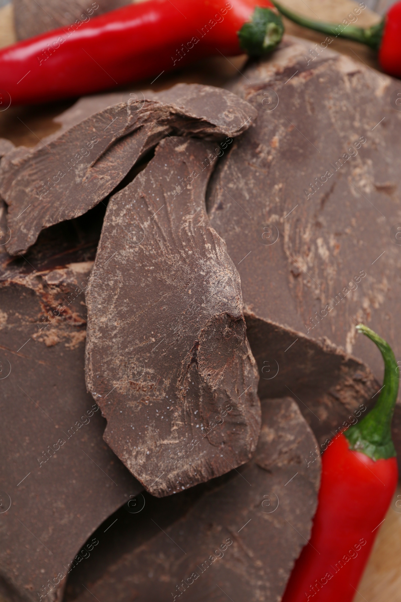 Photo of Pieces of tasty chocolate with chili peppers on table, closeup