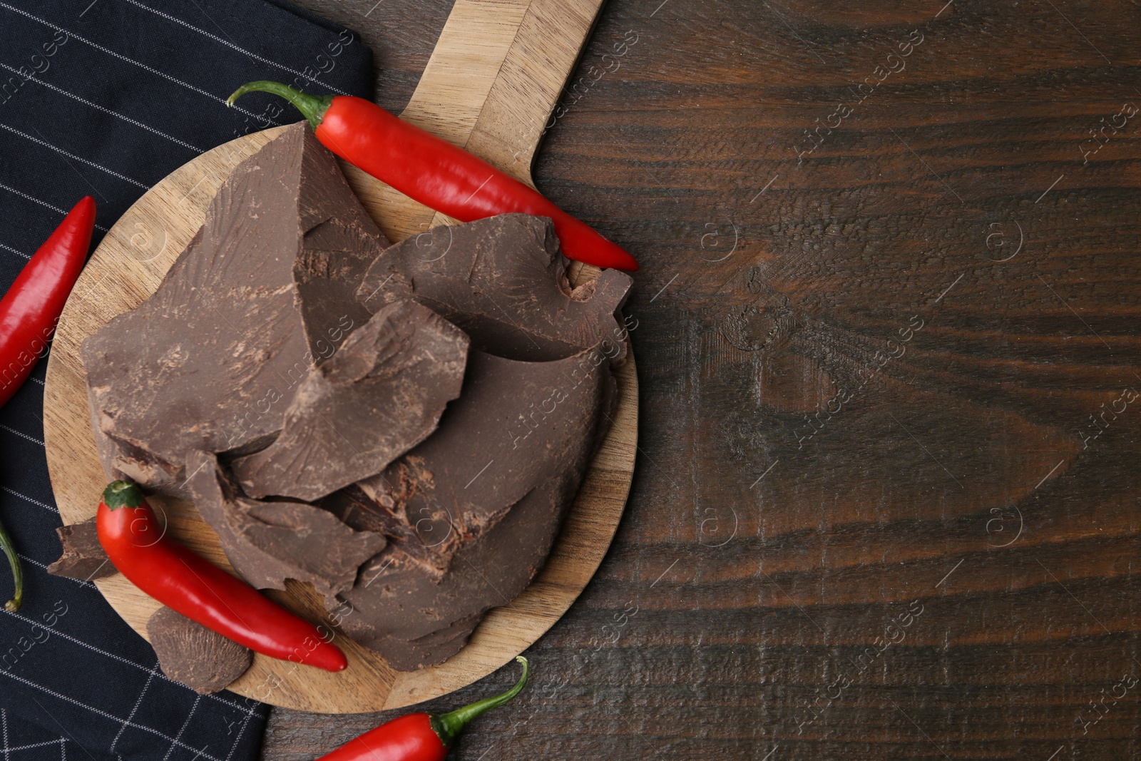 Photo of Pieces of tasty chocolate with chili peppers on wooden table, flat lay. Space for text