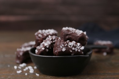 Photo of Tasty chocolate candies with salt in bowl on wooden table, closeup