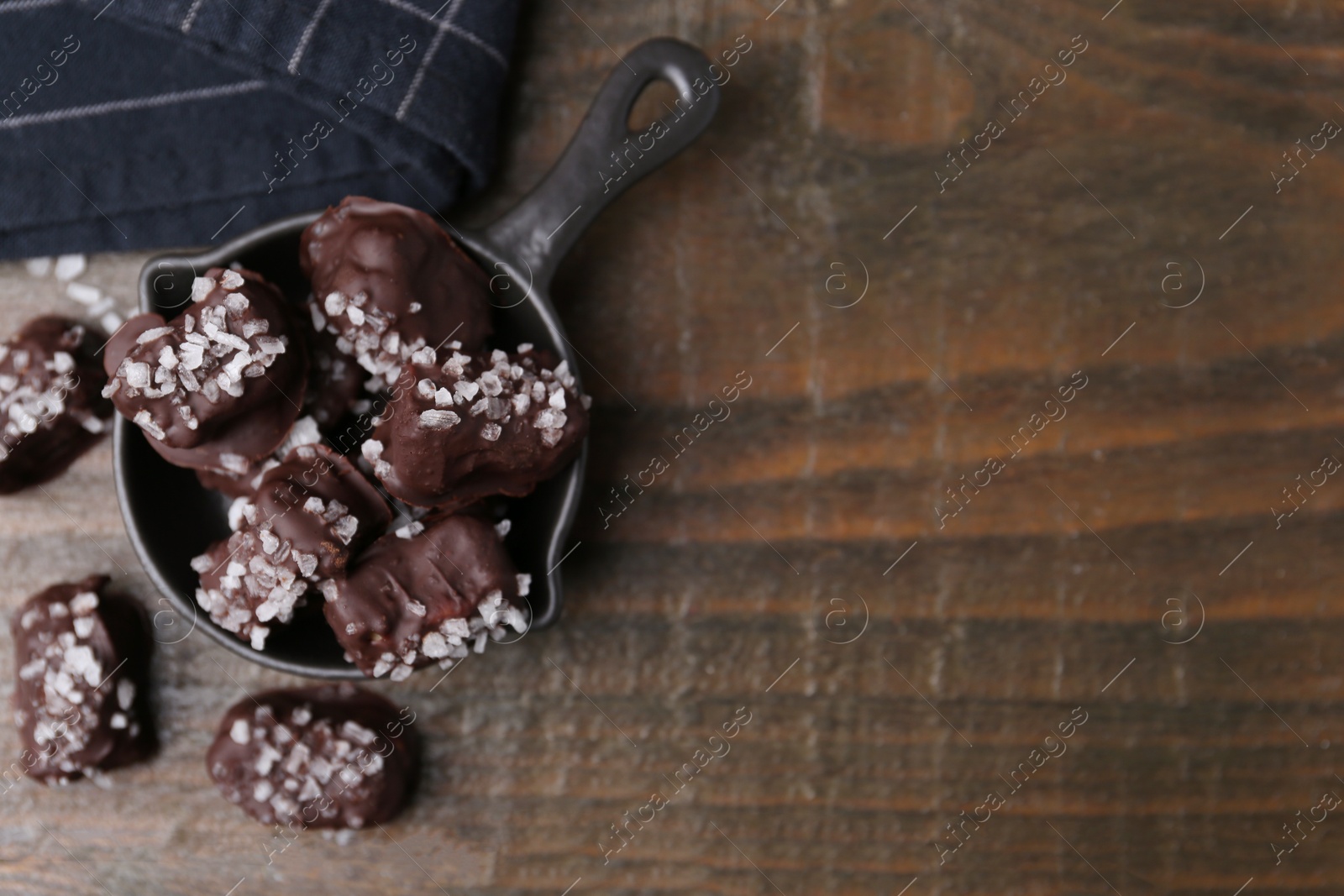 Photo of Tasty chocolate candies with salt on wooden table, flat lay. Space for text