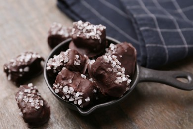 Photo of Tasty chocolate candies with salt on wooden table, closeup