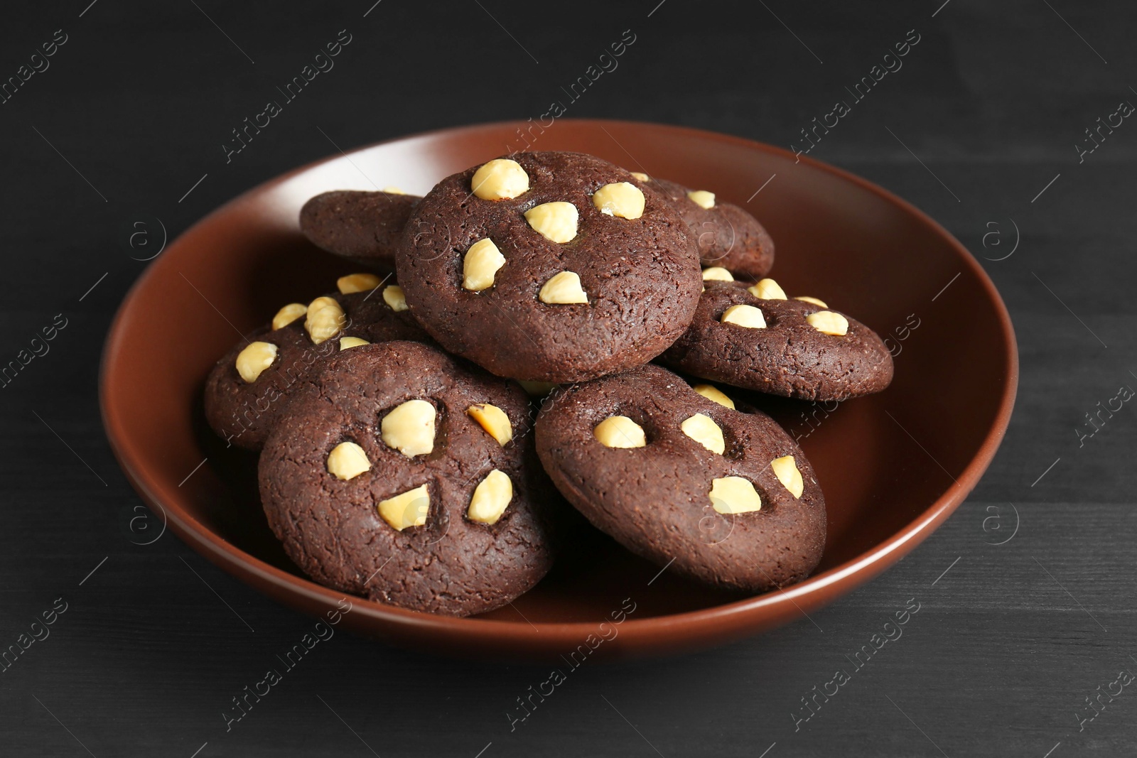 Photo of Delicious chocolate cookies with hazelnuts on black wooden table, closeup