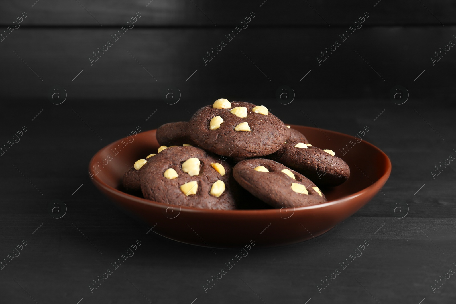 Photo of Delicious chocolate cookies with hazelnuts on black wooden table, closeup