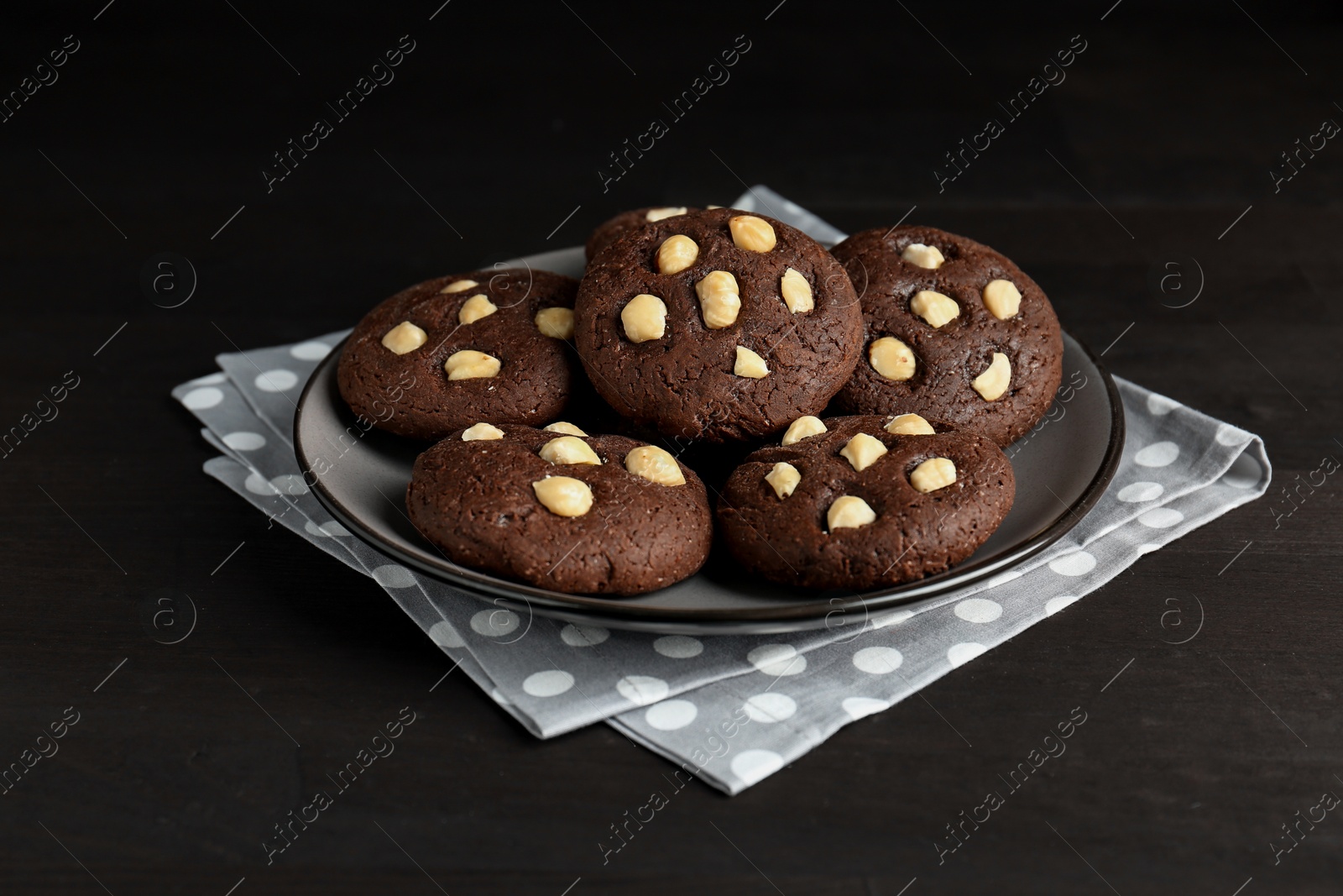 Photo of Delicious chocolate cookies with hazelnuts on black wooden table