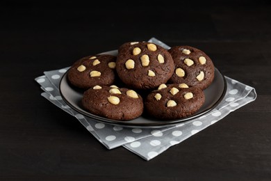 Photo of Delicious chocolate cookies with hazelnuts on black wooden table