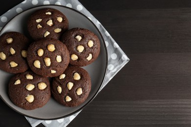 Photo of Delicious chocolate cookies with hazelnuts on black wooden table, top view. Space for text