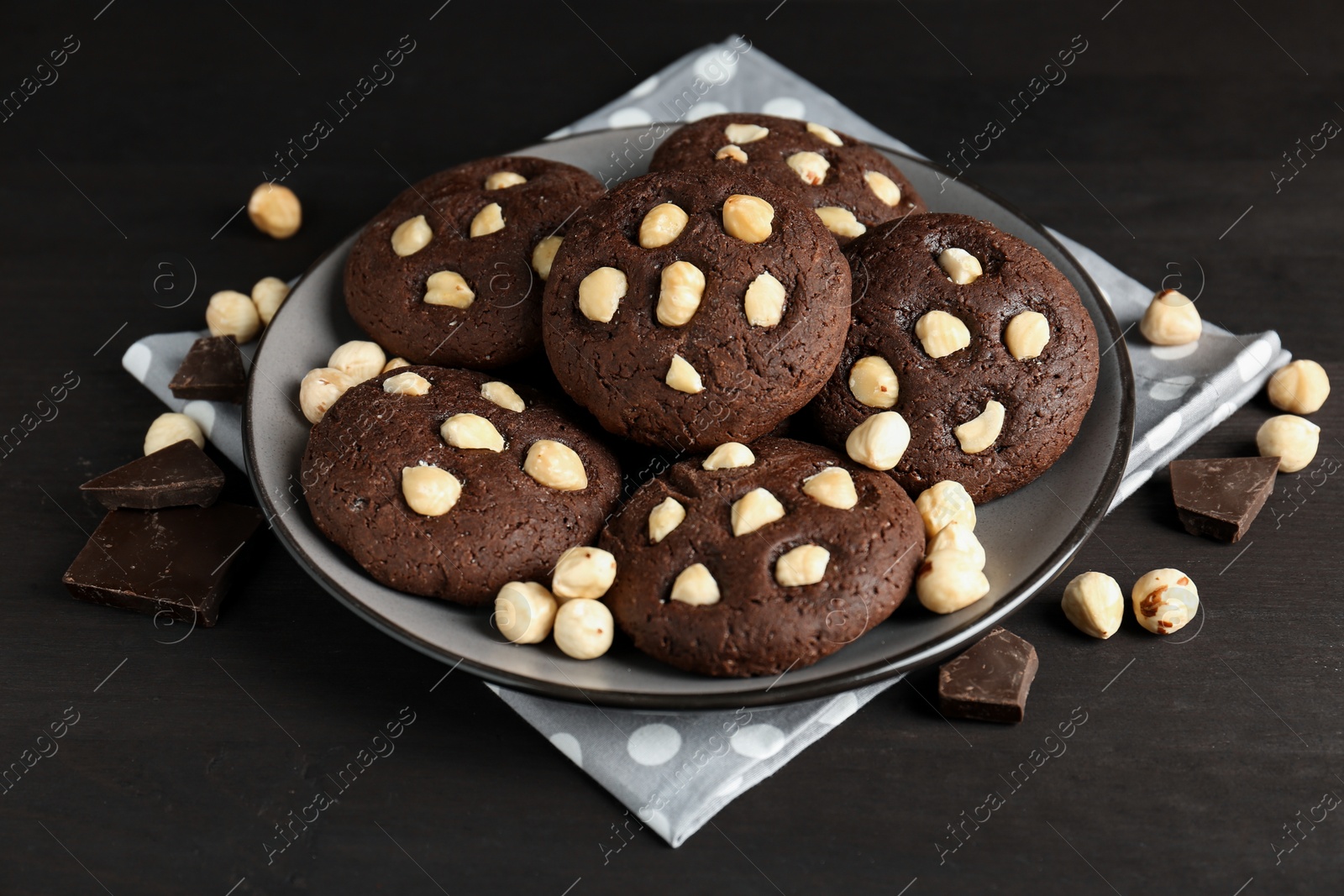 Photo of Delicious chocolate cookies with hazelnuts on black wooden table, closeup