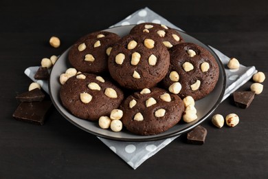 Photo of Delicious chocolate cookies with hazelnuts on black wooden table, closeup