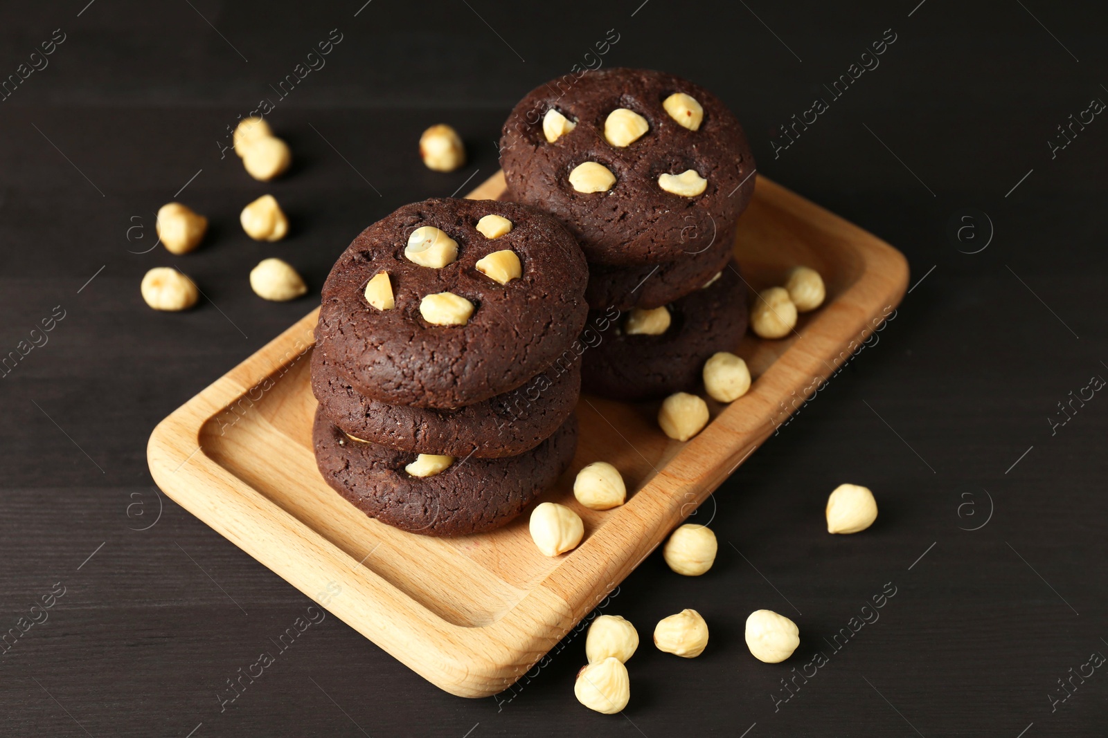 Photo of Delicious chocolate cookies with hazelnuts on black wooden table, closeup