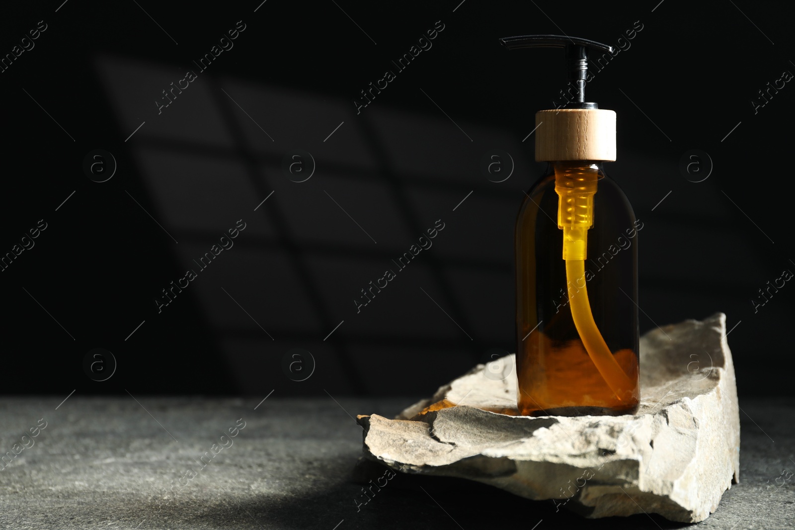 Photo of Bottle of cosmetic product and rock on grey table, space for text